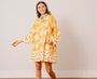 Woman wearing a yellow and white patterned dress standing against a plain background