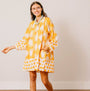 Woman wearing a yellow and white patterned dress standing against a plain background