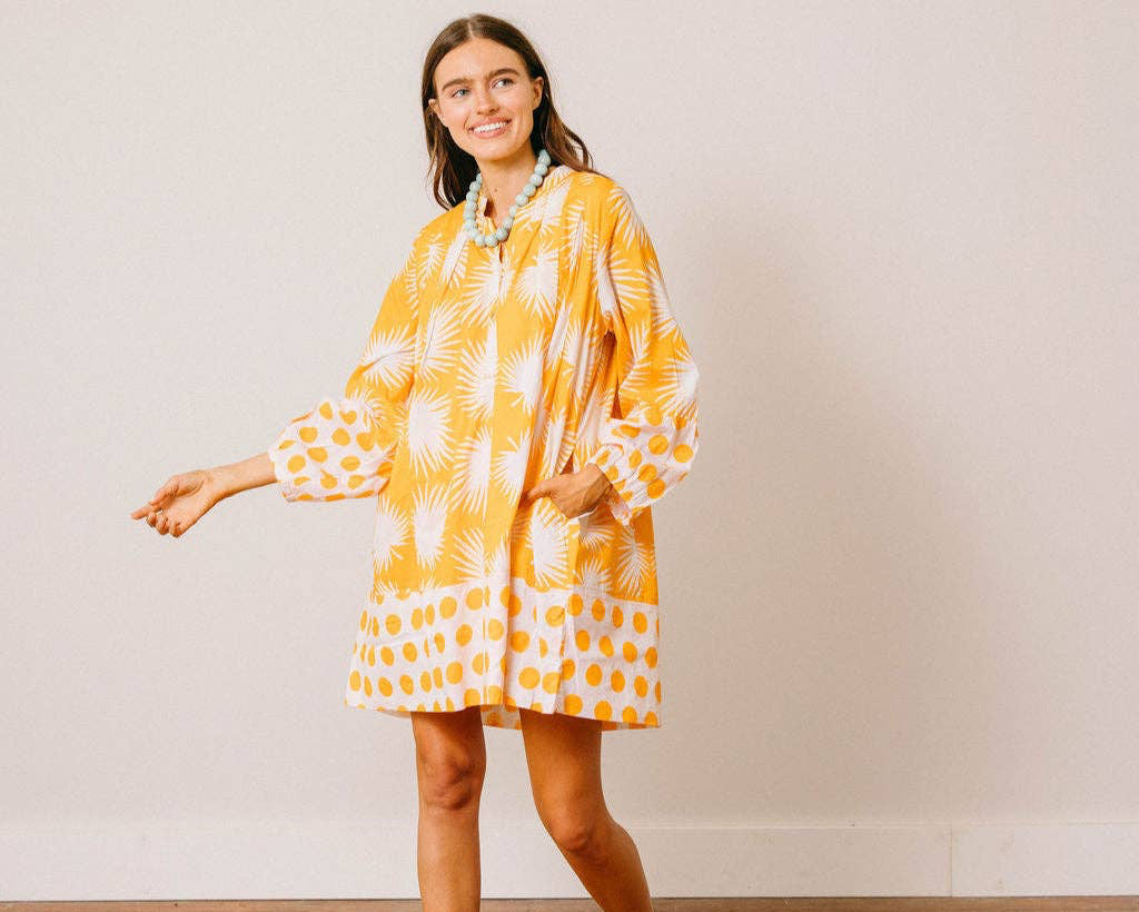 Woman wearing a yellow and white patterned dress standing against a plain background