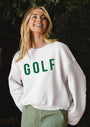 Woman wearing a white sweatshirt with 'GOLF' printed in green, standing against a dark background.