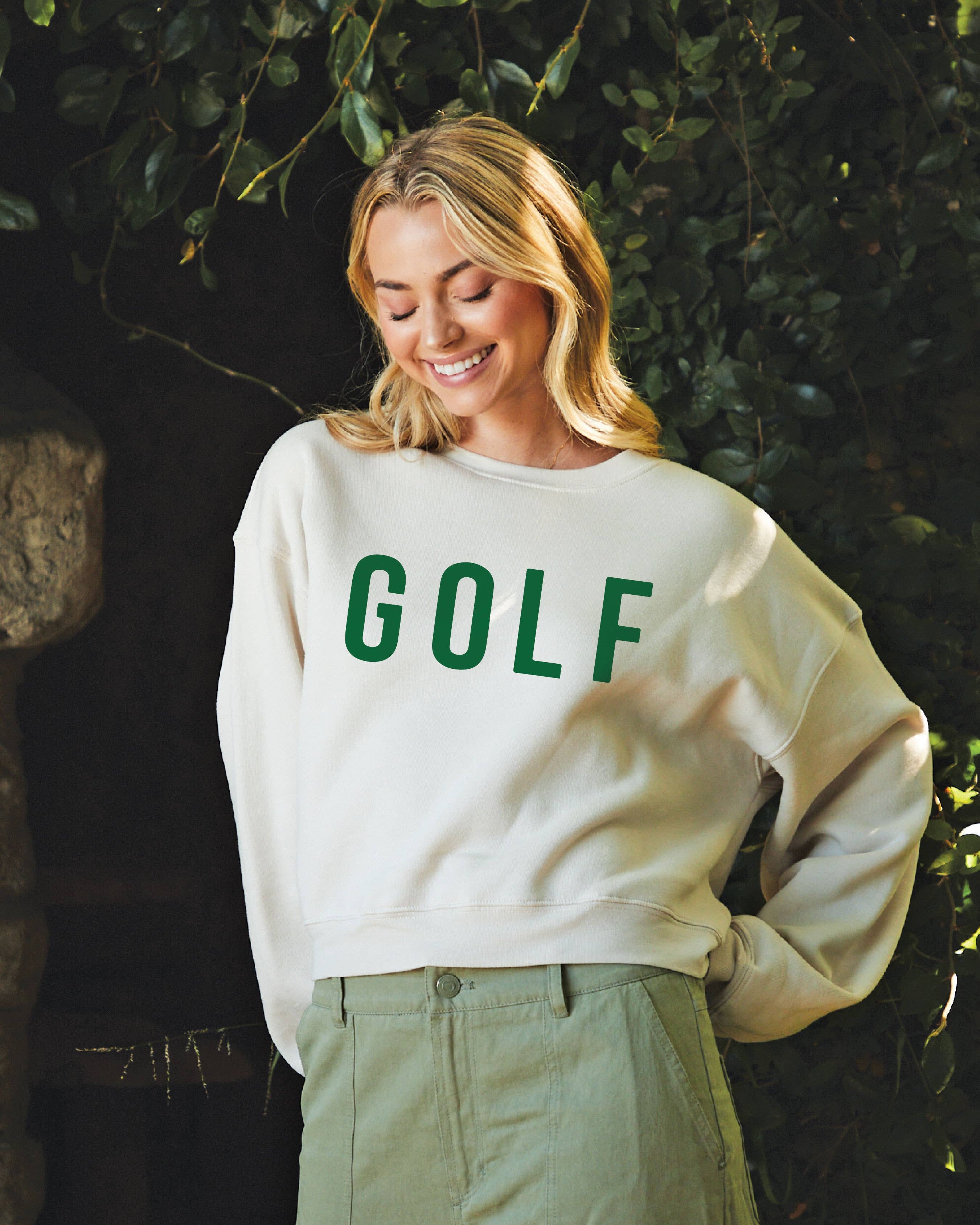 Person wearing a white sweatshirt with 'GOLF' printed in green, standing outdoors.