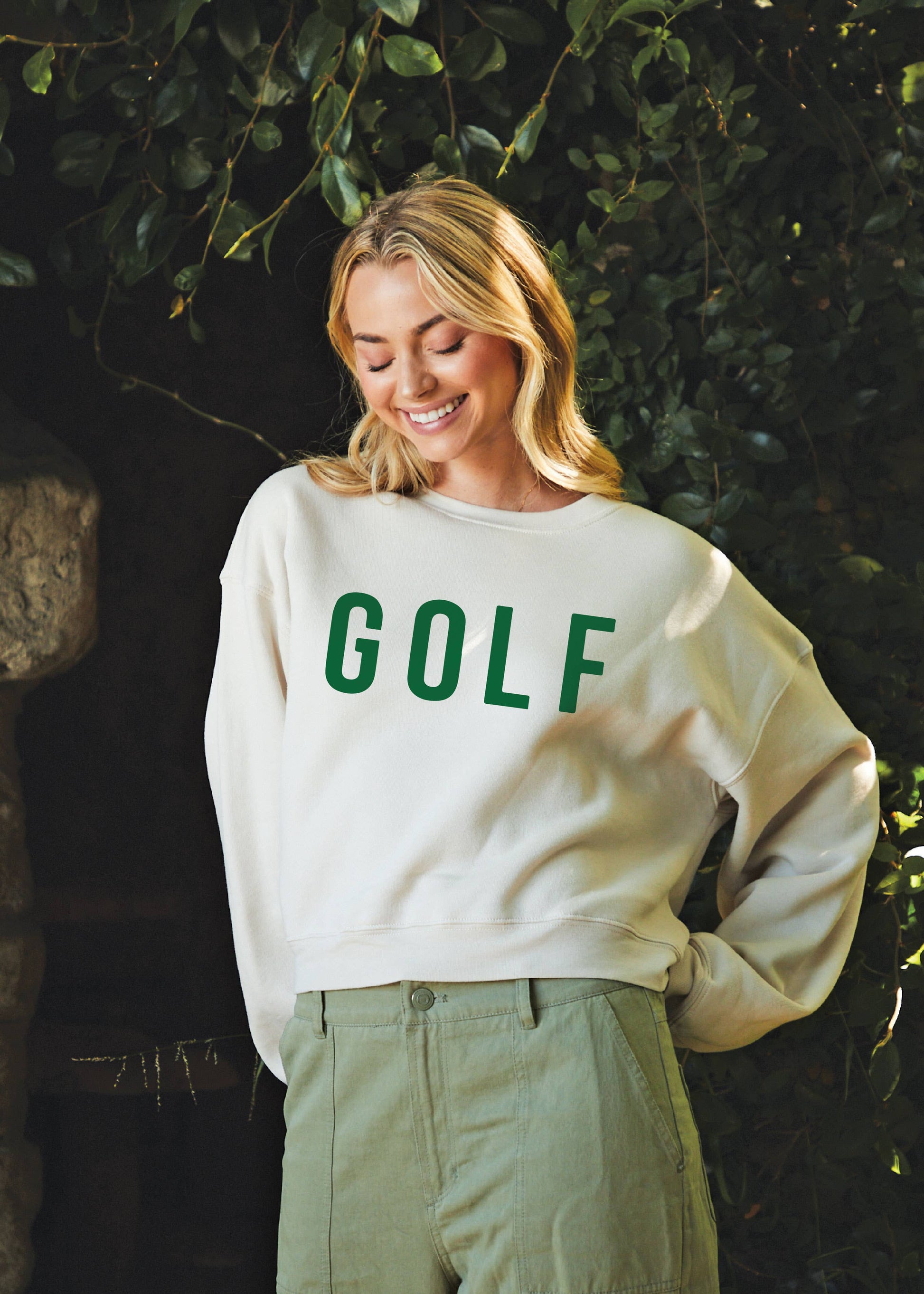 Person wearing a white sweatshirt with 'GOLF' printed in green, standing outdoors.